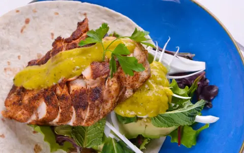 Delicioso wrap de pollo con aguacate, lechugas variadas y salsa verde, servido en un plato azul vibrante.