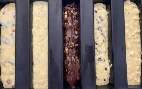 Cinq moules à cake longs prêts pour la cuisson : un aux fruits rouges, un aux amandes, un au chocolat, un aux pépites de chocolat et un aux pommes. Recette 5 cakes longs sucrés.