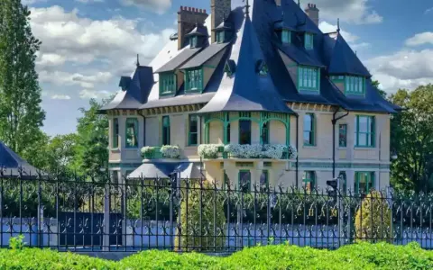 La villa Demoiselle à Reims, une demeure d'exception avec ses toits bleus et ses ornements verts, se dresse fièrement derrière une grille ouvragée.