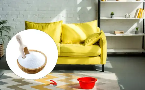 Un divano giallo brillante pronto per essere pulito con bicarbonato. Una ciotola di bicarbonato con un mestolo è in primo piano.