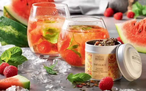 Rafraîchissante recette thé glacé : deux verres remplis de glaçons, fruits rouges et menthe, accompagnés de pastèque et d'une boîte de thé.