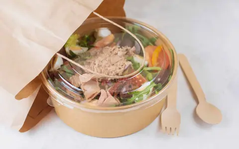 Ensalada de atún para llevar, con ingredientes frescos y cubiertos en un recipiente ecológico. Perfecta para tu licencia take away.