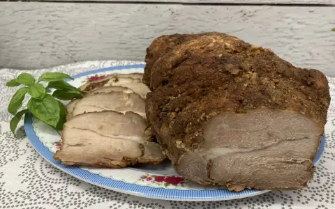 Soczysta łopatka pieczona w rękawie, pokrojona w plastry, z gałązką bazylii na talerzu.