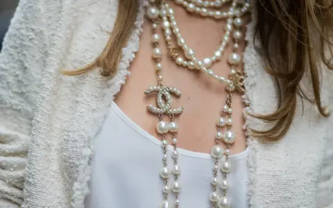Eleganckie stylizacje z perłami, w tym wielowarstwowy naszyjnik Chanel z logo marki i perłami, dodają blasku białej bluzce i żakietowi.