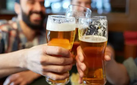 Trzech przyjaciół wznosi toast. Każdy trzyma w dłoni szklankę złocistego piwa z pianką.