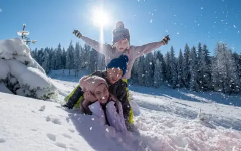 Niños felices en trineo, disfrutando de las vacaciones de invierno cuando empiezan. Nieve cayendo, sol brillante y árboles nevados.