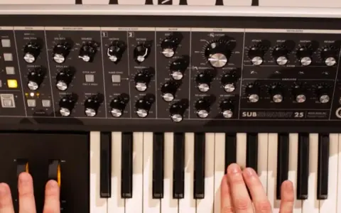 Dłonie grają na klawiaturze syntezatora Moog Subsequent 25, tworząc dźwięki.