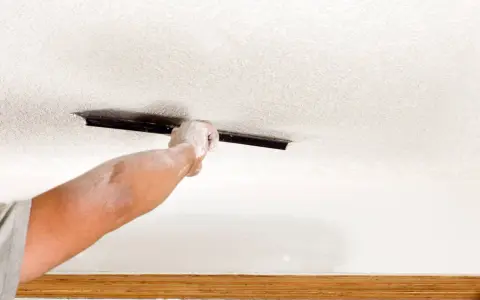 A dusty hand uses a trowel to texture a ceiling, demonstrating how to texture a ceiling for a fresh look.