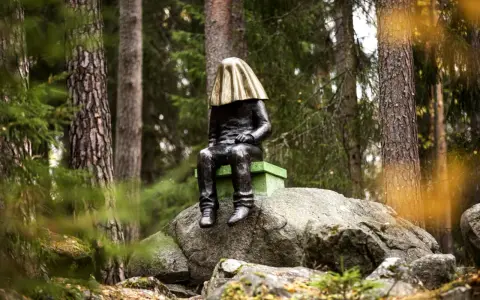En mystisk staty med gyllene tyg över huvudet sitter på en sten i **stadsparken Falun**.