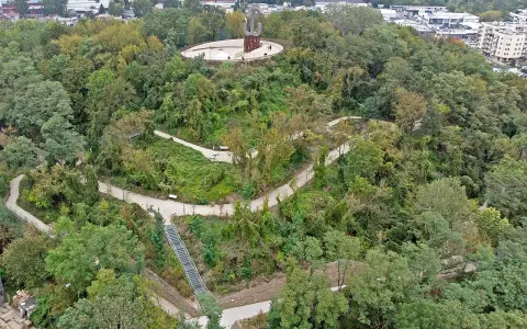 Wzgórze z pomnikiem Kotwicy, otoczone zielenią. Kręte ścieżki i schody prowadzą przez park akcji "Burza", oferując widok na miasto i Wisłę.
