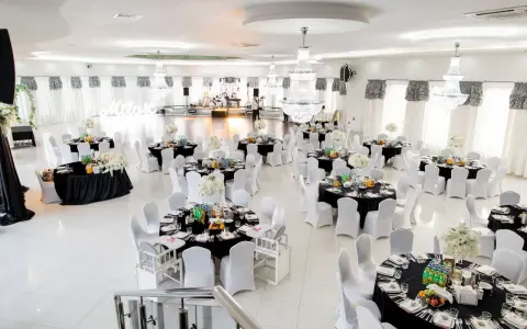 Elegancka sala weselna z czarnymi obrusami i białymi pokrowcami na krzesła. Stoły zastawione, gotowe na przyjęcie gości. Zastanawiasz się, ile za talerzyk na weselu?
