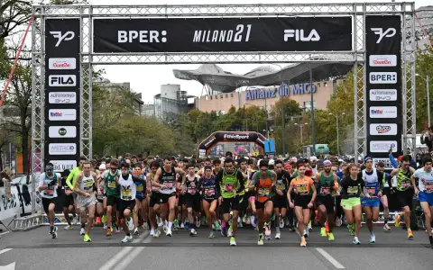Corredores listos para la media maratón Milán 2021. La carrera arranca bajo un arco con patrocinadores y el logo de Fila.