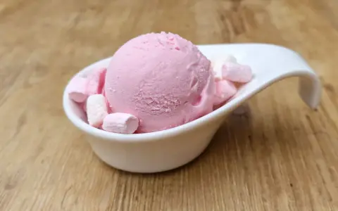 Eine Kugel rosa Bubble Gum Eiscreme mit Marshmallows in einer weißen Schale auf Holzhintergrund.