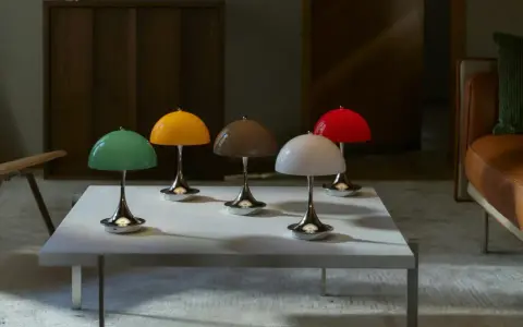 Fem färgglada lampor i Verner Panton-stil står på ett vitt bord. En brun soffa och en läderfåtölj syns i bakgrunden.