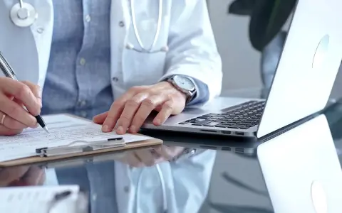 Lekarz w białym kitlu pisze na dokumentach, obok laptop. Zastanawia się, ile można być na zwolnieniu lekarskim od psychiatry.