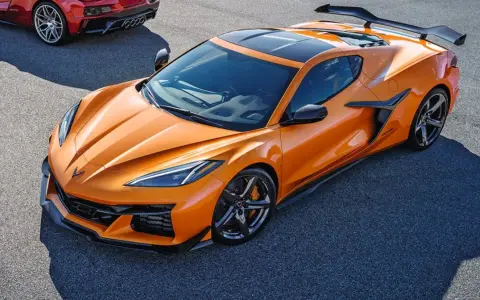 Pomarańczowy Chevrolet Corvette C8 z czarnym dachem i spojlerem na torze wyścigowym. Obok widać fragment czerwonego samochodu.