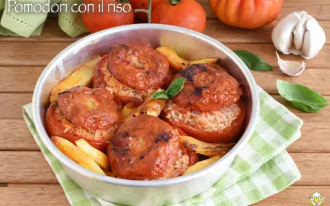 Pomodori ripieni di riso, cotti al forno con patate e basilico. Un piatto estivo saporito e colorato.