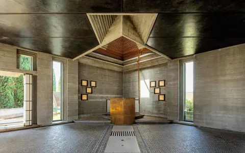 Interno moderno con altare dorato, pareti in cemento grezzo e soffitto a punta. Un esempio di architetti famosi italiani.