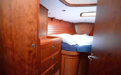 Gemütliches Bett mit gestreifter Bettwäsche im Innenbereich einer Segelyacht. Holzverkleidung und Schränke schaffen eine warme Atmosphäre.