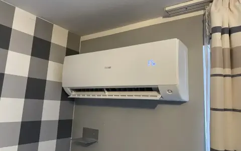 Biała klimatyzacja Haier zamontowana na szarej ścianie, obok wzorzystej tapety i zasłon.