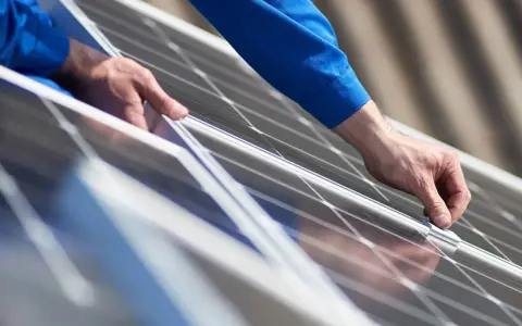 Händer i blå arbetskläder monterar solpaneler från Longi Solar på ett tak.