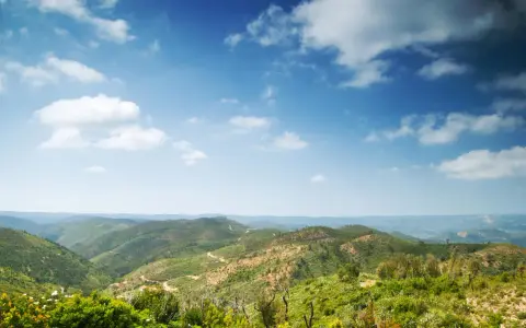 Grüne Hügel und Täler in Monchique, Portugal, unter einem weiten Himmel mit weißen Wolken.