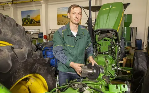 Mechanik z częścią John Deere, być może szuka informacji o john deere kody serwisowe, aby naprawić traktor.