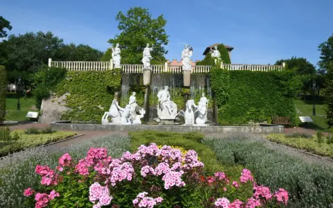 Prachtvoller Brunnen mit Skulpturen und Wasserfällen, umgeben von blühenden Blumen und Grün im botanischen Garten NRW.
