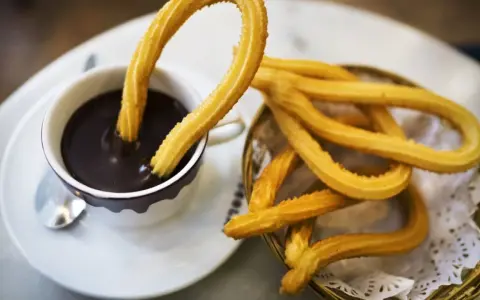 Churros sin gluten dorados y crujientes, uno sumergido en chocolate caliente, otro en una cesta.
