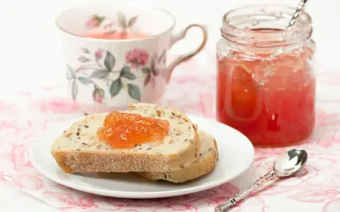 Fetta di pane con marmellata di anguria, tazza da tè fiorita e barattolo di marmellata.
