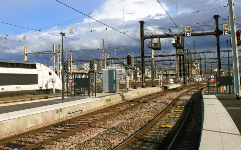 Ein weißer Hochgeschwindigkeitszug steht am Bahnsteig. Die Gleise führen in die Ferne, vorbei an Signalen und Oberleitungen. Vielleicht ist dies der **Zug nach Barcelona**?