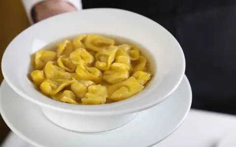 Un piatto fumante di tortellini in brodo, un classico comfort food italiano, servito in una ciotola bianca.