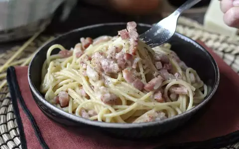 Un tenedor recoge espaguetis cremosos con trozos de bacon crujiente, creando un delicioso plato de pasta con bacon.