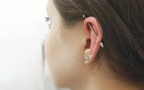 Industrialny piercing ucha z długą sztangą i dwoma stożkami. To przykład, co to jest piercing, który ozdabia ciało.