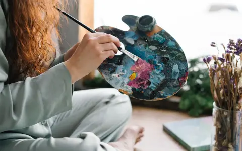 Une artiste aux cheveux roux mélange des couleurs vives sur sa palette, prête à peindre. Apprenez comment utiliser la peinture acrylique pour créer de telles œuvres.