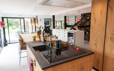 Îlot de cuisine moderne avec plan de travail en granit, évier noir et plaque à induction. La **rénovation cuisine bois massif** se révèle dans les placards et l'îlot central.