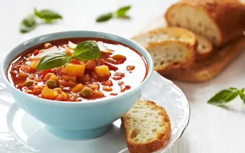 Zupa jarzynowa a minestrone w niebieskiej miseczce, udekorowana bazylią, podana z chrupiącym pieczywem.