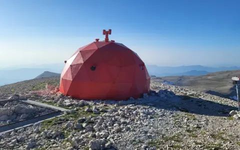 Struttura rossa a cupola su un terreno roccioso, con vista panoramica sulle montagne del Monte Amaro.
