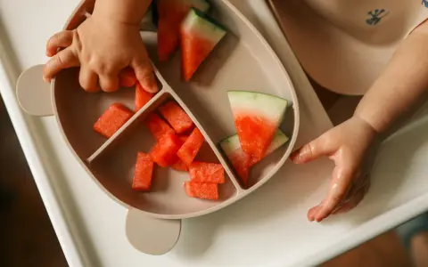 Kleine Hände greifen nach saftigen Wassermelone-Stücken auf einem Teller. Ein süßer Wassermelone-Baby-Moment.