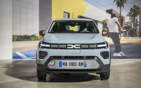 Jasnoszary dacia elektryk z miedzianymi lusterkami. Z przodu logo Dacia i tablica rejestracyjna MA-080-AM 92.