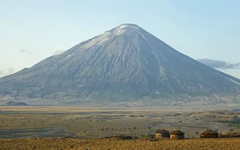Ol Doinyo Lengai, wulkan w Tanzanii, góruje nad sawanną z kilkoma tradycyjnymi chatami Masajów.