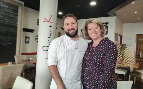 Le chef et sa collègue sourient devant la colonne "Authentik St Grégoire". L'ambiance chaleureuse du restaurant est palpable.