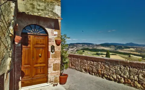 Un portone in legno in un borgo toscano, con vista panoramica sulle colline. Perfetto per un tour in moto tra i borghi più belli della Toscana.