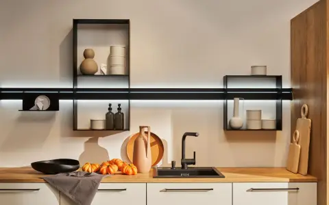Cocinas sin muebles altos, con estantes flotantes y decoración minimalista. Encimera de madera con fregadero negro, jarrones y calabazas.