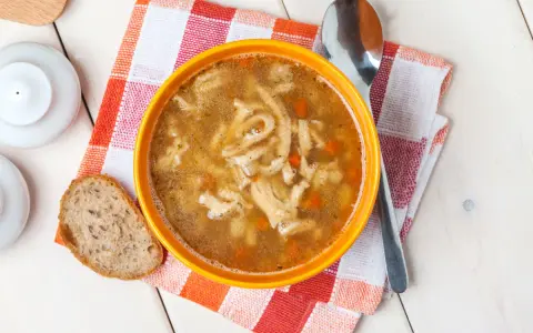 Aromaticzne flaki po zamojsku w pomarańczowej misce, obok kromka chleba i łyżka. Pyszne danie gotowe do spożycia.