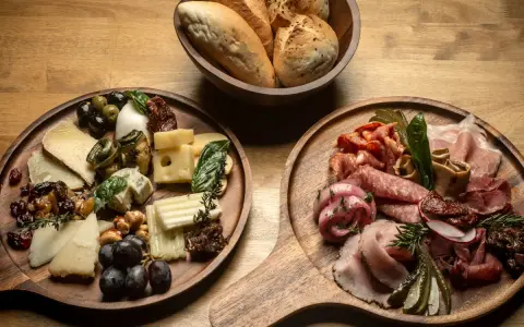 Deska serów i wędlin inspiracje: bogactwo smaków i aromatów na drewnianych deskach, z pieczywem w tle.