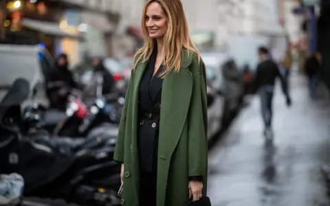 Mujer con traje negro y un abrigo verde olivo, ideal para saber qué abrigo llevar con traje mujer.