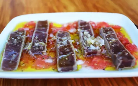 Tiras de atún marinado sobre rodajas de tomate y cítricos, un delicioso plato de comida típica de Huelva.