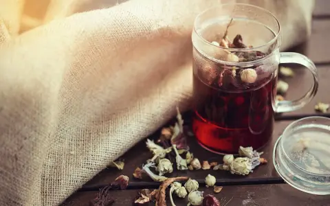 Infusion rouge dans une tasse en verre, entourée d'herbes séchées. Un remède naturel diurétique à portée de main.