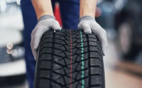 Ręce w rękawiczkach trzymają nową oponę, pokazując jej głęboki bieżnik. Idealna na każdą drogę, sprawdzamy, ile bieżnika ma nowa opona.